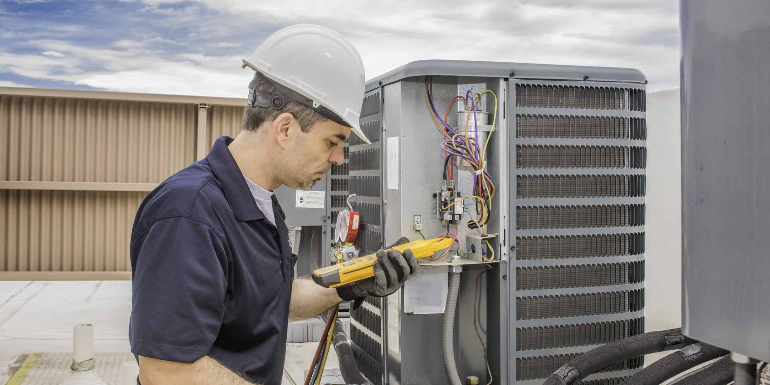 Trained hvac technician holding a voltage meter, performing preventative maintenance on a air conditioning condenser unit.
